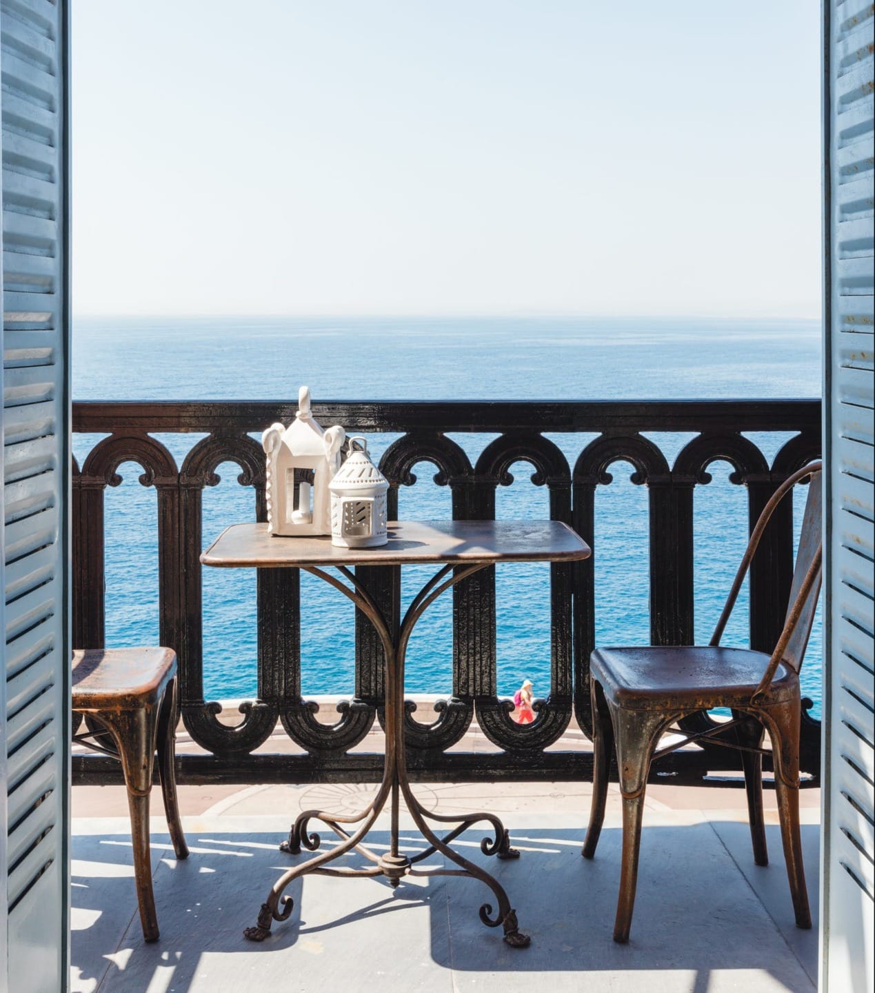 Balcony with metal table and chairs overlooking a calm ocean view on a clear day.
