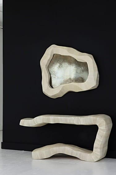 Abstract beige console table with matching organic-shaped mirror on black wall background.