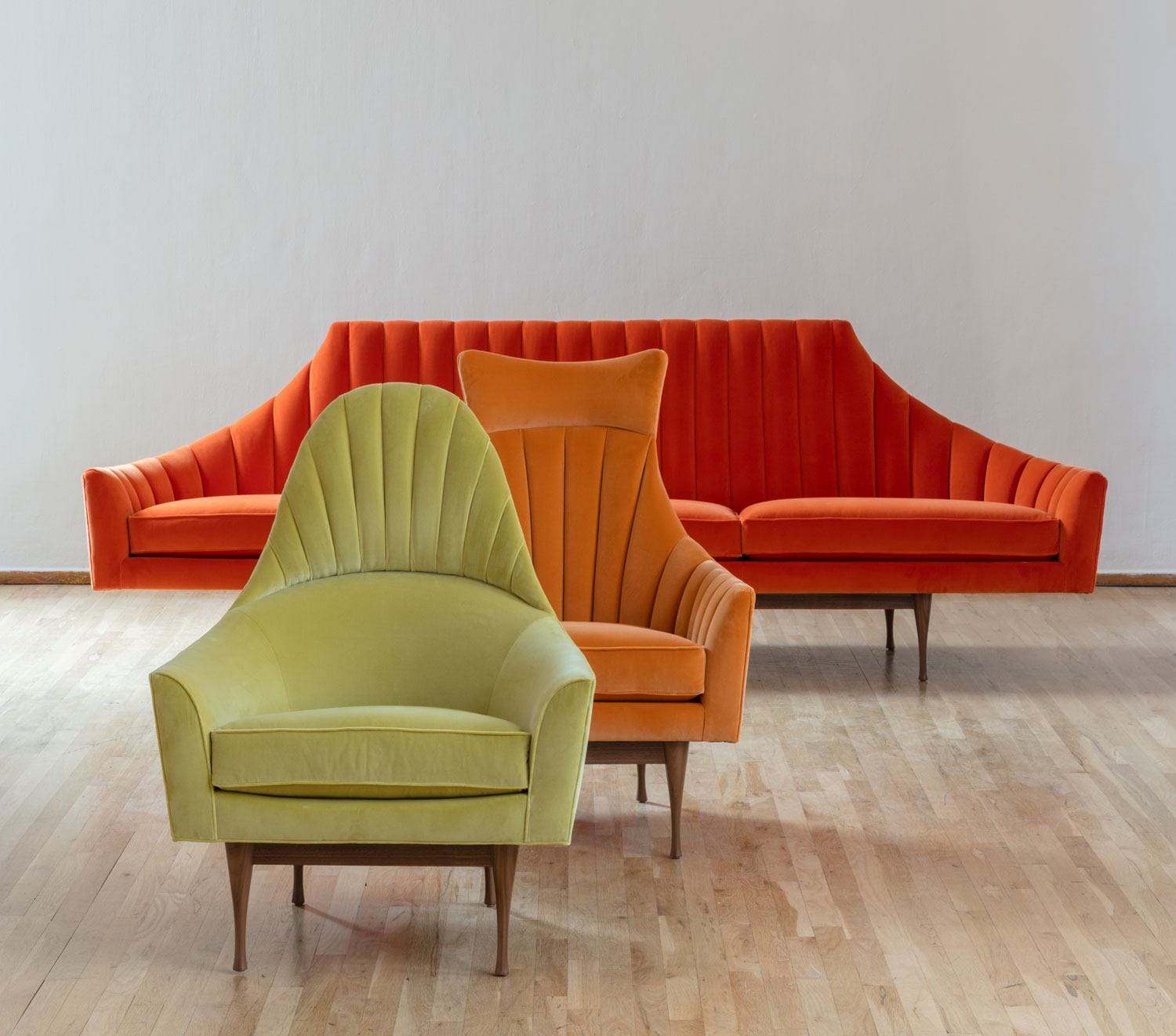 Mid-century modern furniture set with an orange sofa and green and orange armchairs on a wooden floor.
