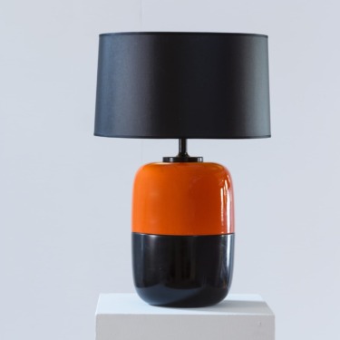 Modern table lamp with a glossy orange and black base and a simple black lampshade on a white pedestal