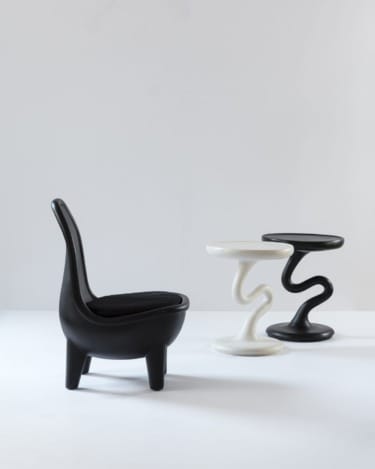 Black modern chair and two abstract end tables, one white and one black, in a minimalist setting.