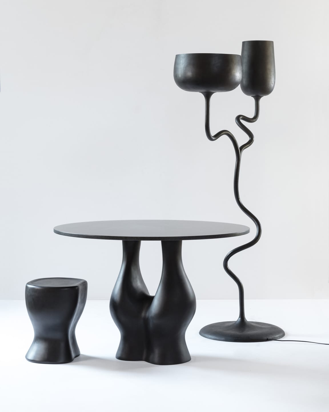Modern black table, stool, and floor lamp with artistic, wavy designs against a white background