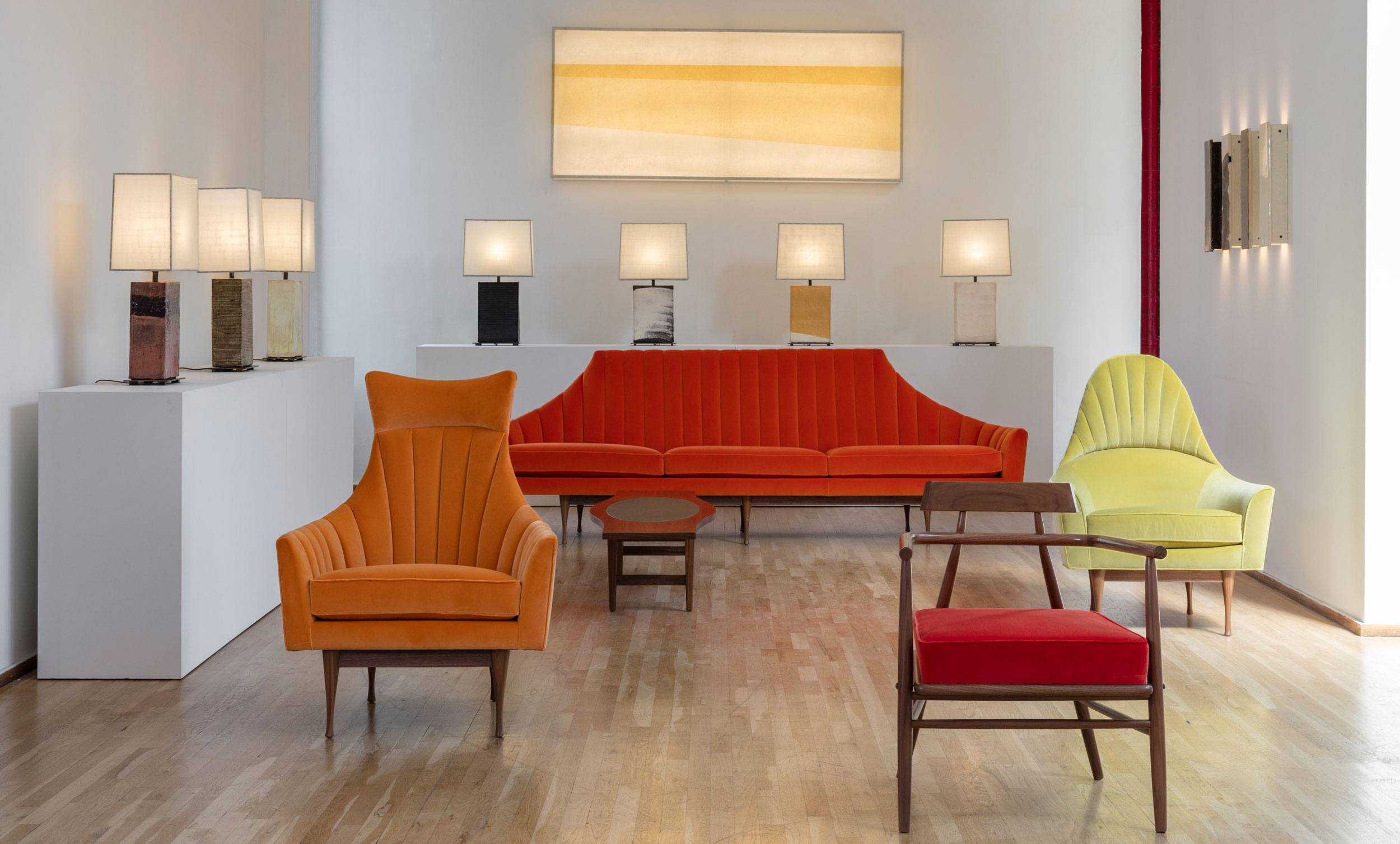 Mid-century modern furniture showroom with orange and yellow chairs, a red sofa, and a row of table lamps on display.