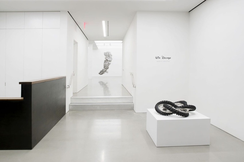 Minimalist art gallery interior with monochrome sculptures and wall art, featuring white walls and a polished floor.