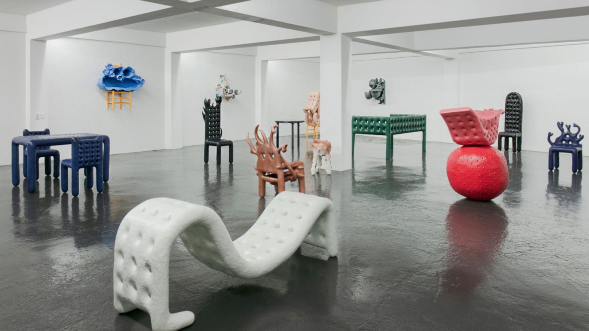 Modern art exhibition featuring abstract, colorful sculptural furniture in a white gallery space with a reflective floor.