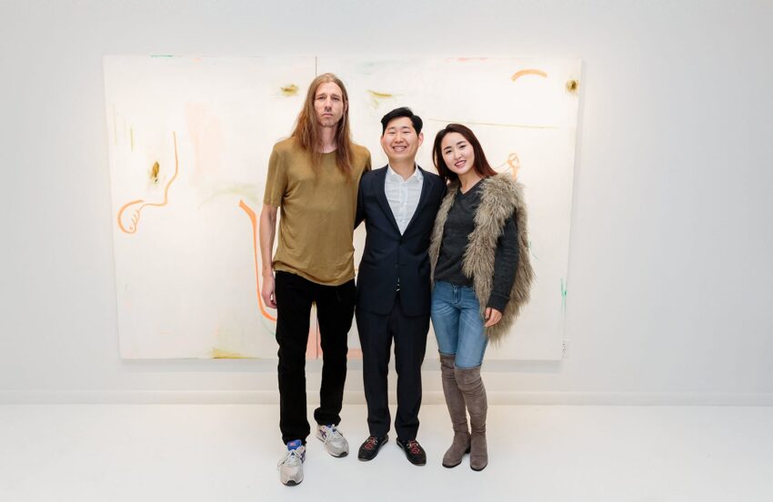 Three people posing in front of an abstract painting in a gallery setting.