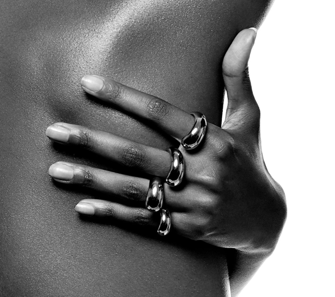 Hand with three metallic rings elegantly gripping a bare shoulder in a black and white close-up photograph.