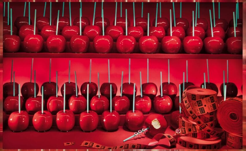 Glossy red candy apples on sticks arranged in rows with red carnival tickets nearby.