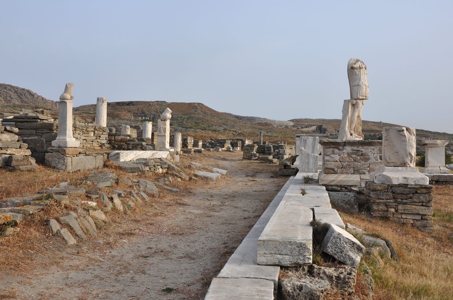 Ancient ruins with stone statues and pathways under a clear sky in a historic archaeological site.