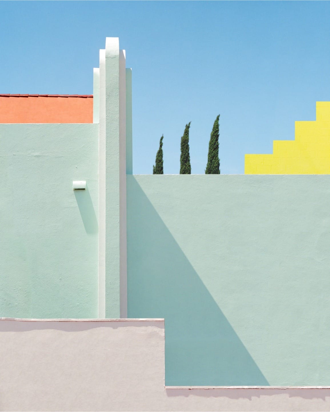 Colorful geometric architecture with pastel walls against clear blue sky and trees in background