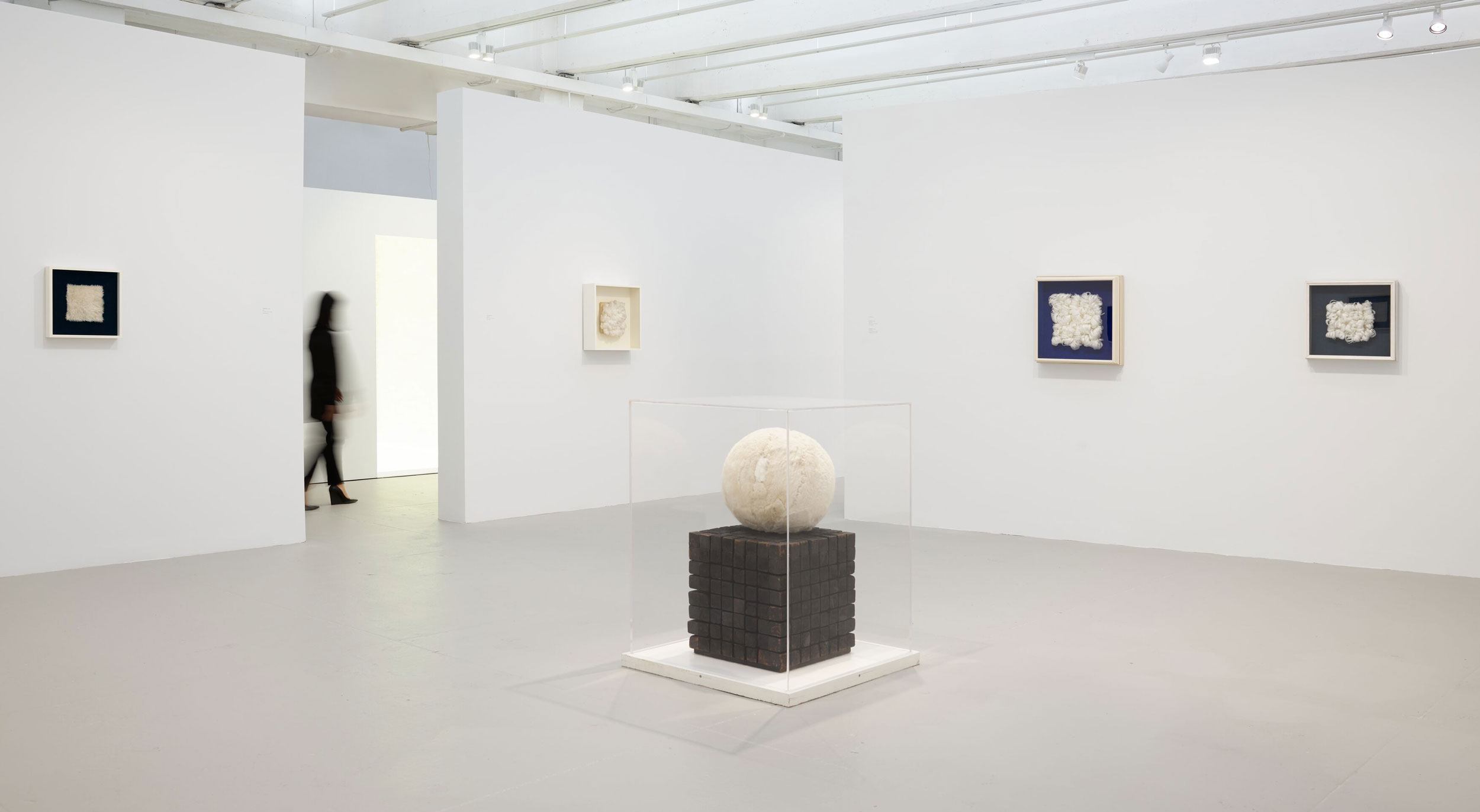 Contemporary art gallery with abstract paintings on white walls and a cube sculpture with a sphere in the foreground.