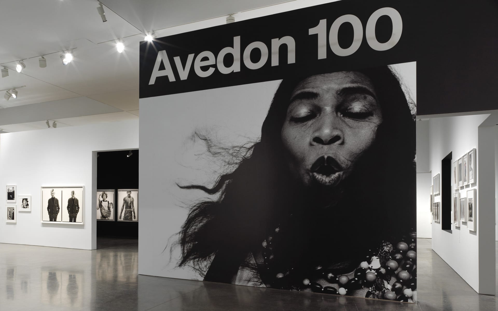 Exhibition display with large black-and-white portrait of a person and the text "Avedon 100" above the image.