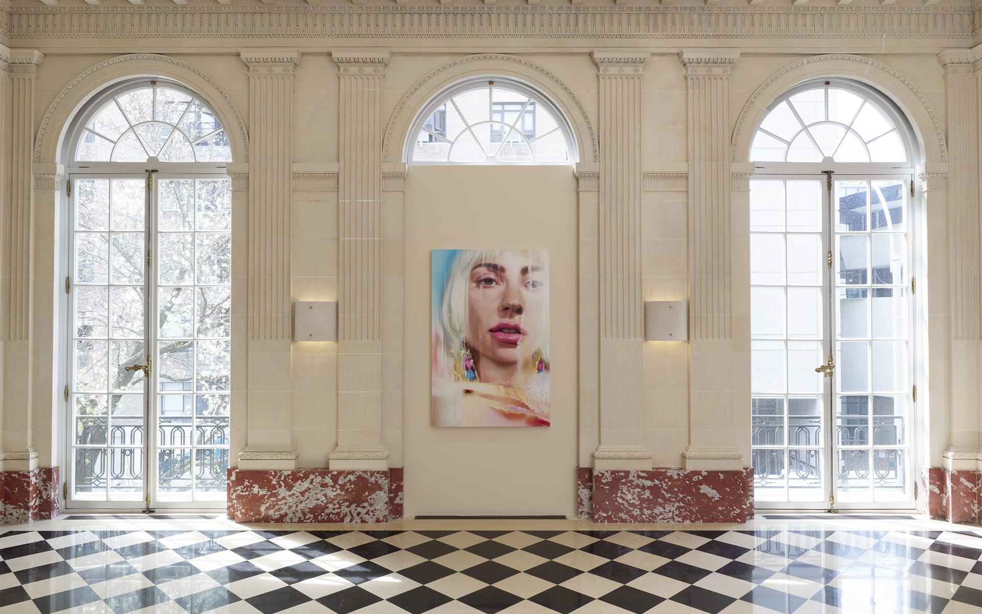 A grand room with arched windows and a colorful portrait on display above a black and white checkered floor.