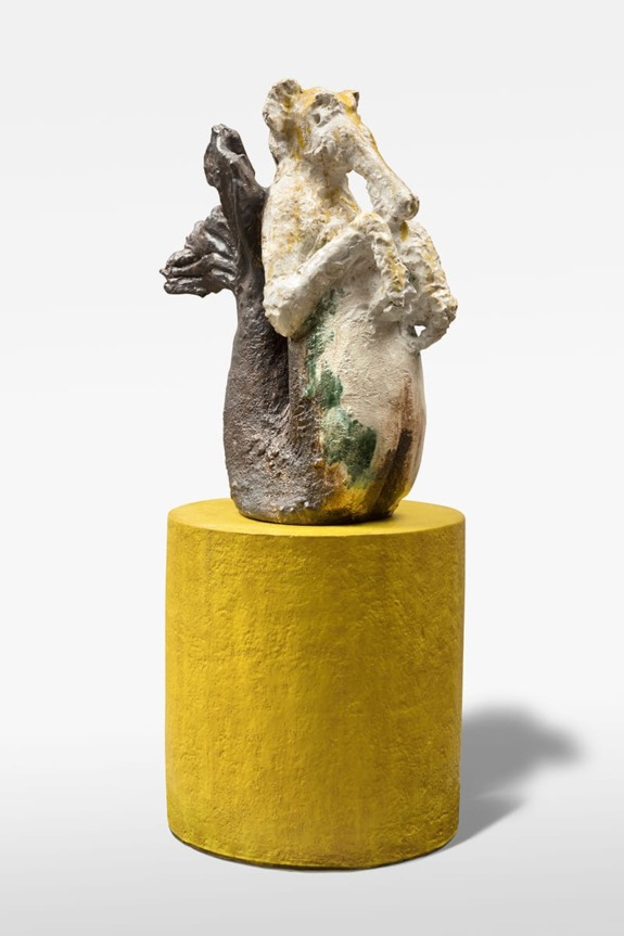 Abstract ceramic sculpture with textured surface on a yellow cylindrical pedestal against a plain background.