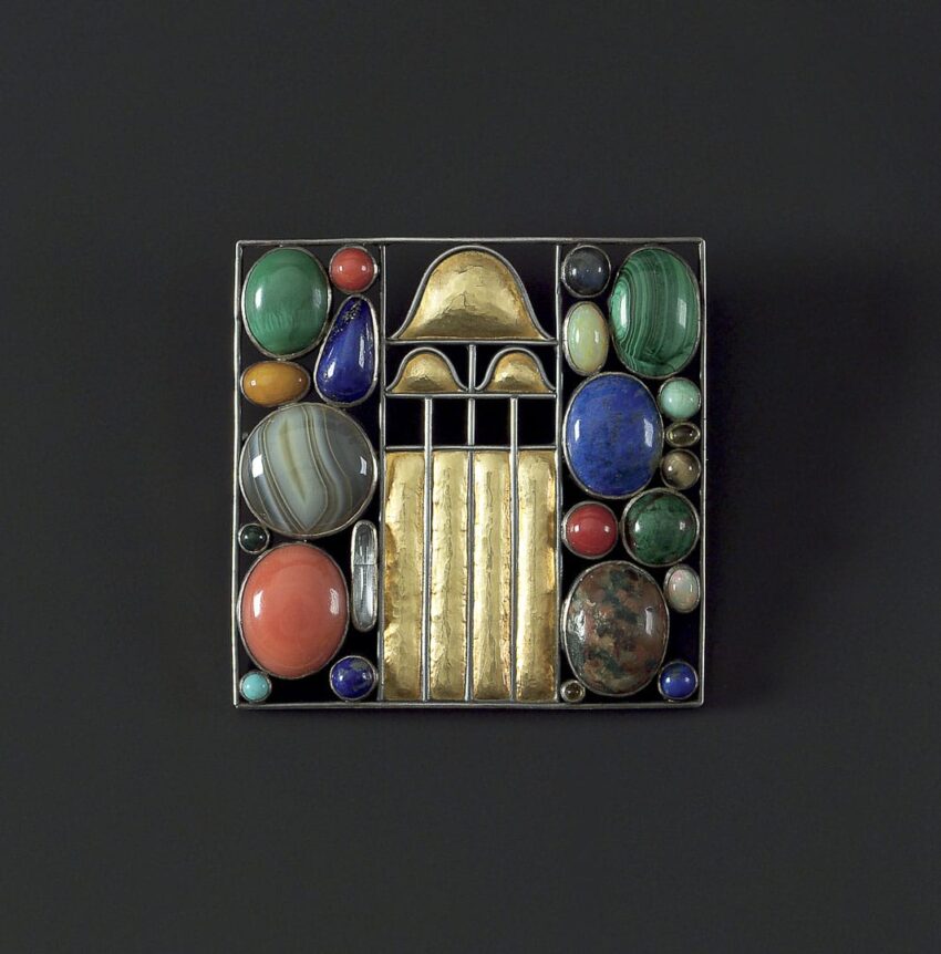 Colorful geometric brooch with various gemstones and a central gold design on a black background.