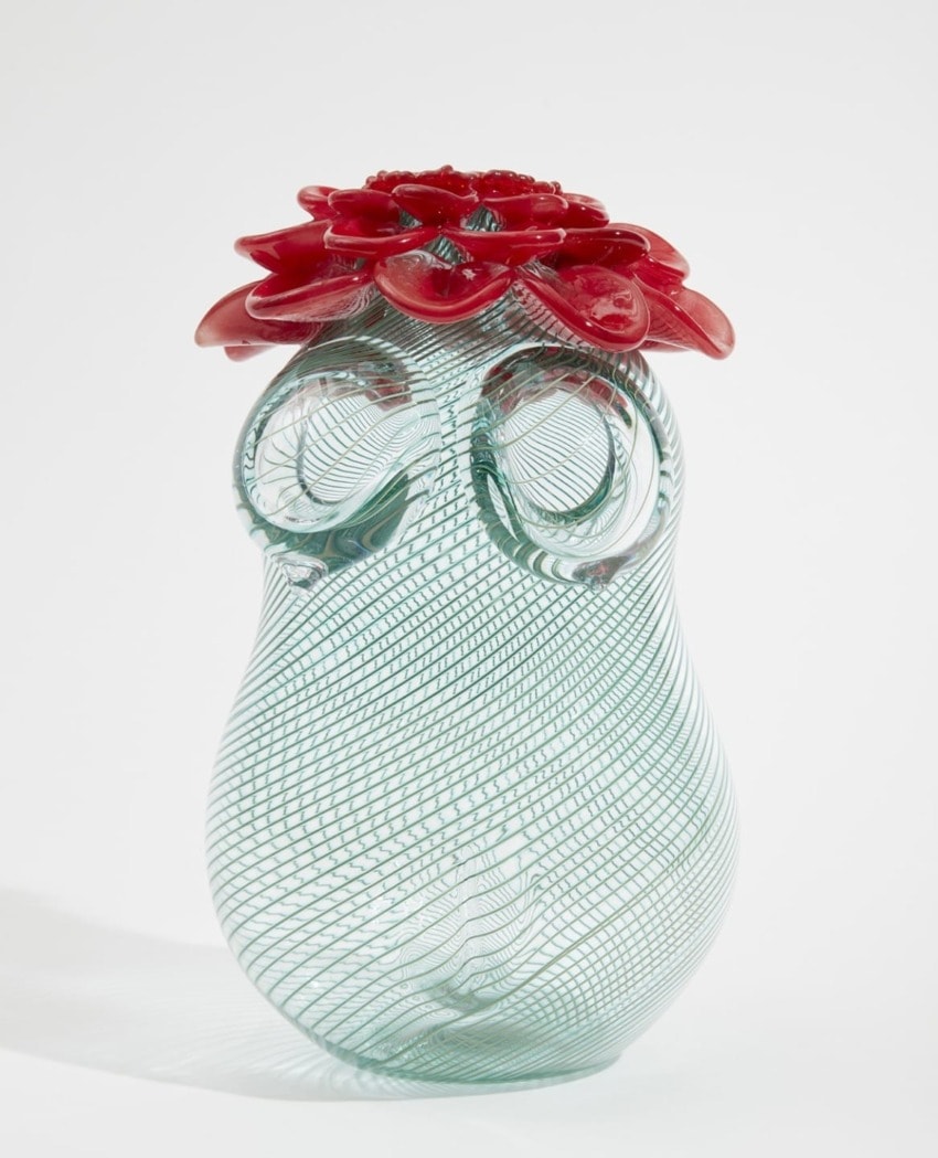 Glass vase with intricate swirling patterns and a vivid red flower on top.