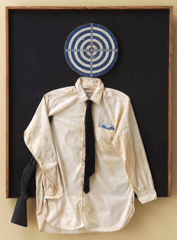 Artistic display of a white shirt with a black tie and rifle beneath a target on a dark background.