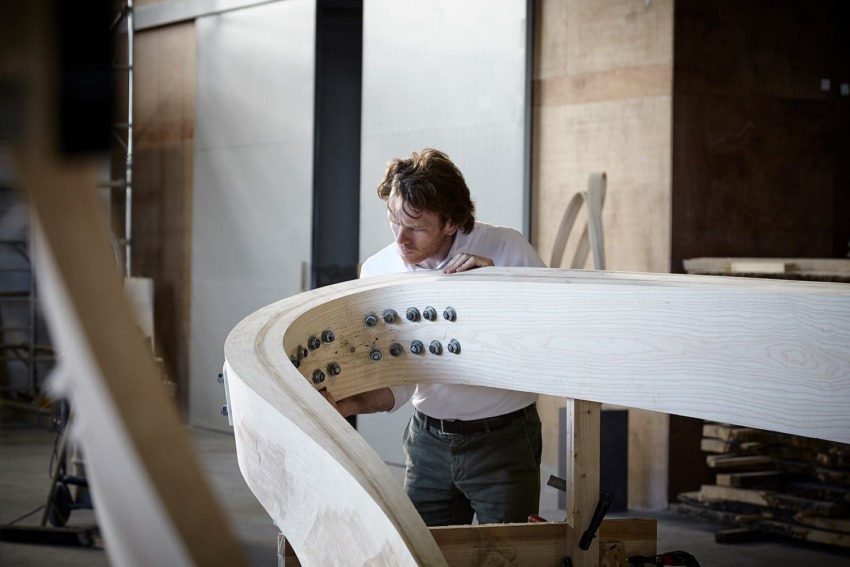 Person inspecting large wooden structure in workshop, focusing on metal bolts and craftsmanship details.