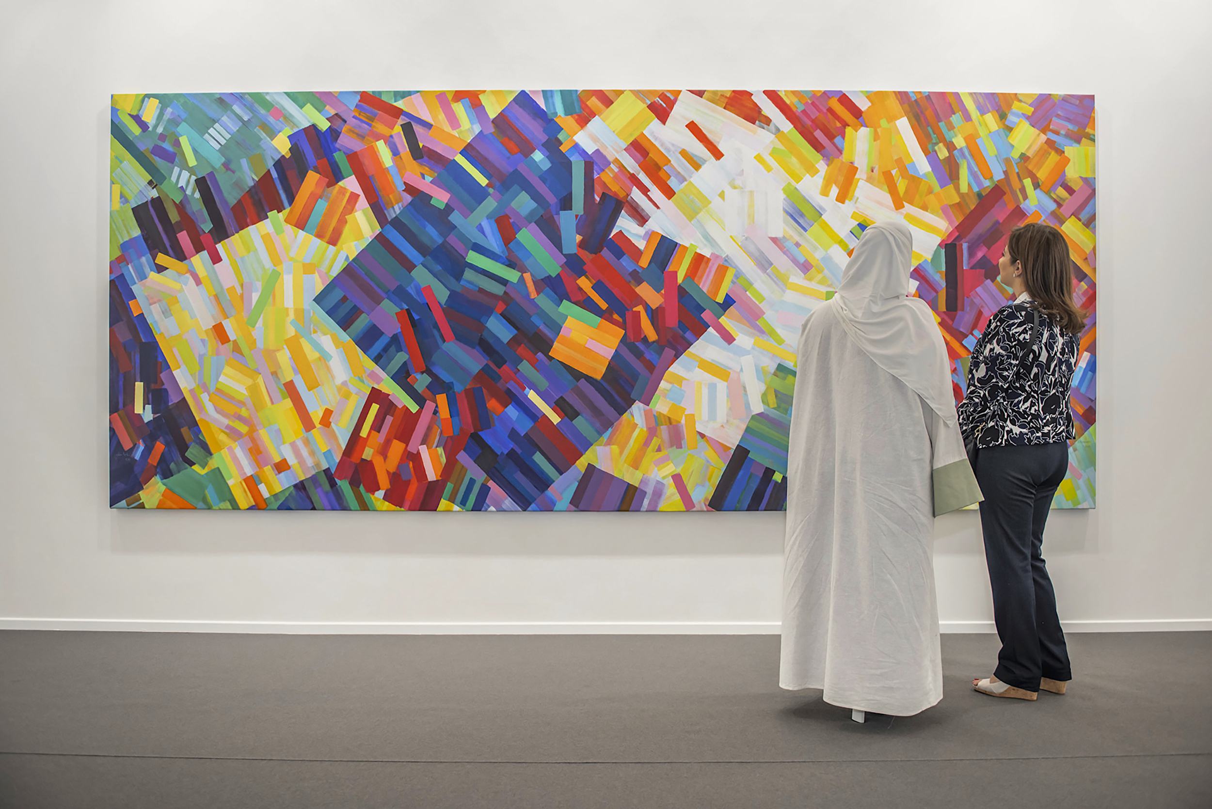 Two people in front of a colorful abstract painting in an art gallery.