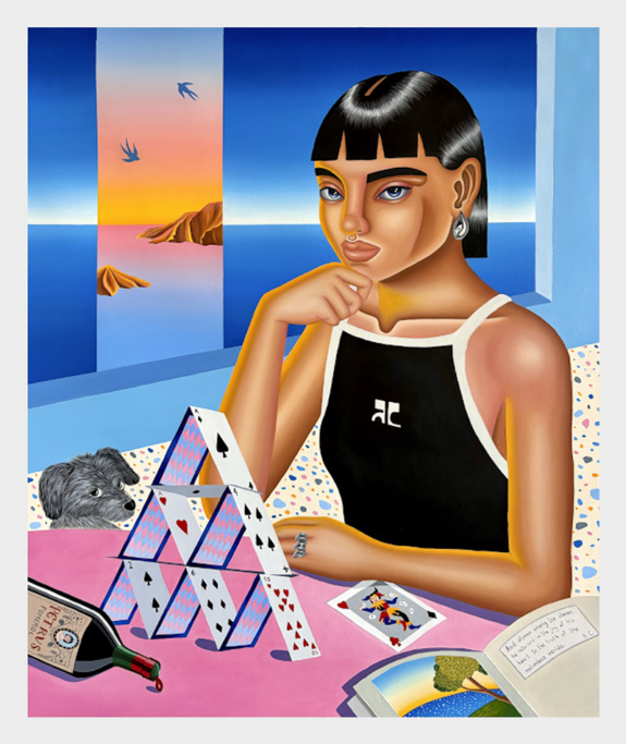 Woman sitting at table with card tower, dog, wine, book, and sunset view.