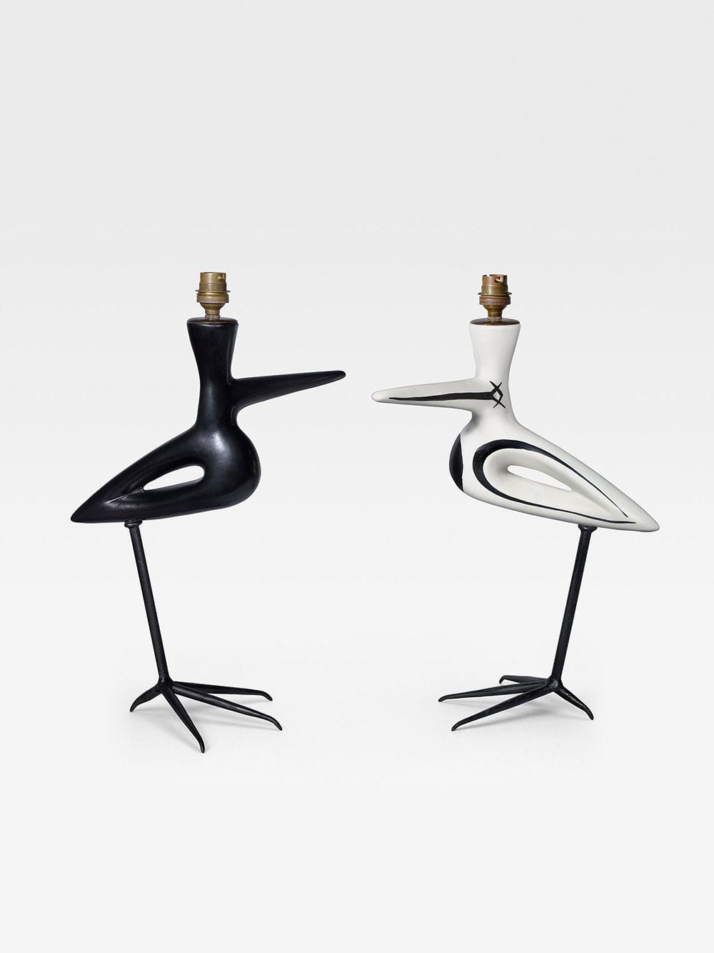 Two abstract bird-shaped lamps, one black and one white, with spindly legs and minimalist design on a plain background.