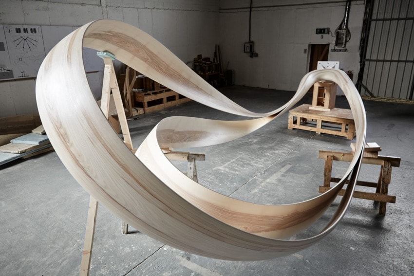 Wooden spiral sculpture in workshop, surrounded by tools and wooden workbenches, displaying craftsmanship and creativity.
