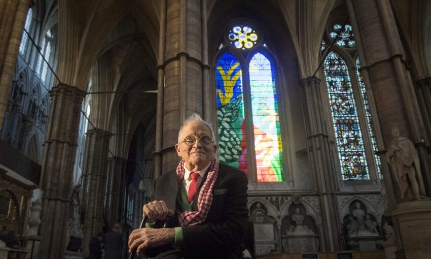 Elderly man sitting in a cathedral with colorful stained glass windows in the background.