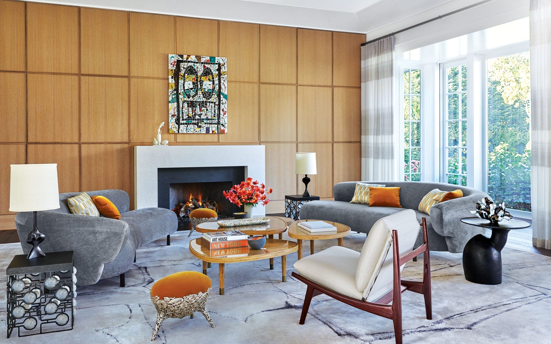 Modern living room with stylish gray sofas, a white fireplace, colorful pillows, and large sunlit windows.