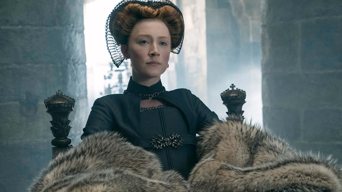 Historical figure in regal attire with fur, sitting on a throne in a dimly lit, stone-walled room.