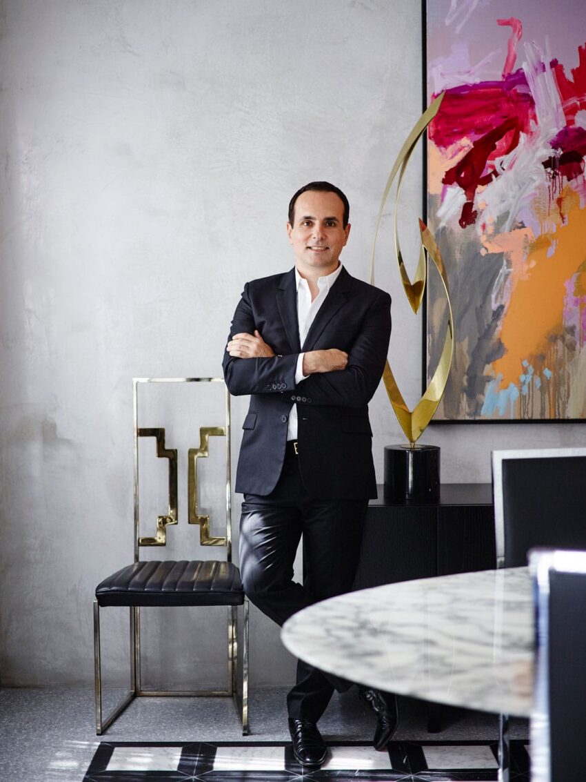 Man in a suit standing by a chair and abstract painting in a modern office setting.