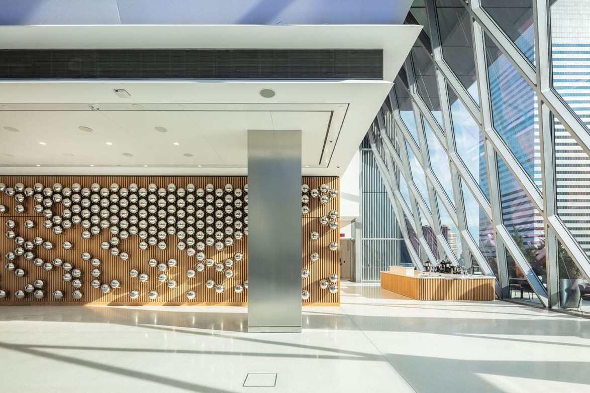 Modern lobby with geometric window design, metal wall art installation, and a small seating area with cityscape views.