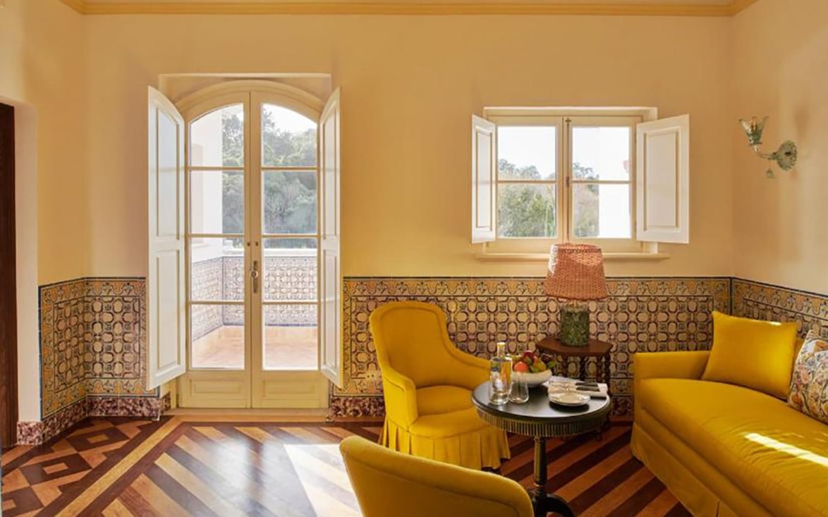 Cozy room with yellow chairs, vintage decor, and open windows overlooking a balcony and lush greenery.