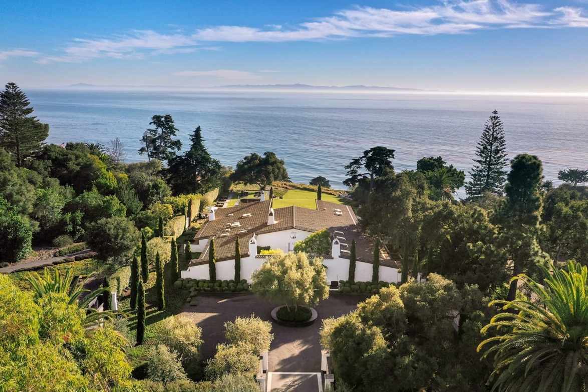 Scenic coastal view with a Mediterranean-style house surrounded by lush greenery, overlooking the ocean.