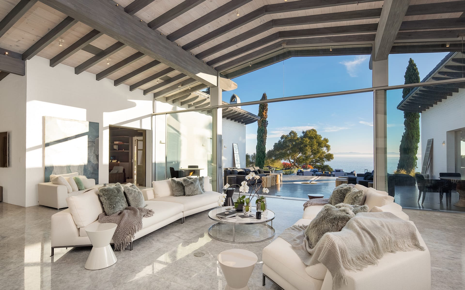 Spacious modern living room with white sofas, glass walls, and stunning ocean view.