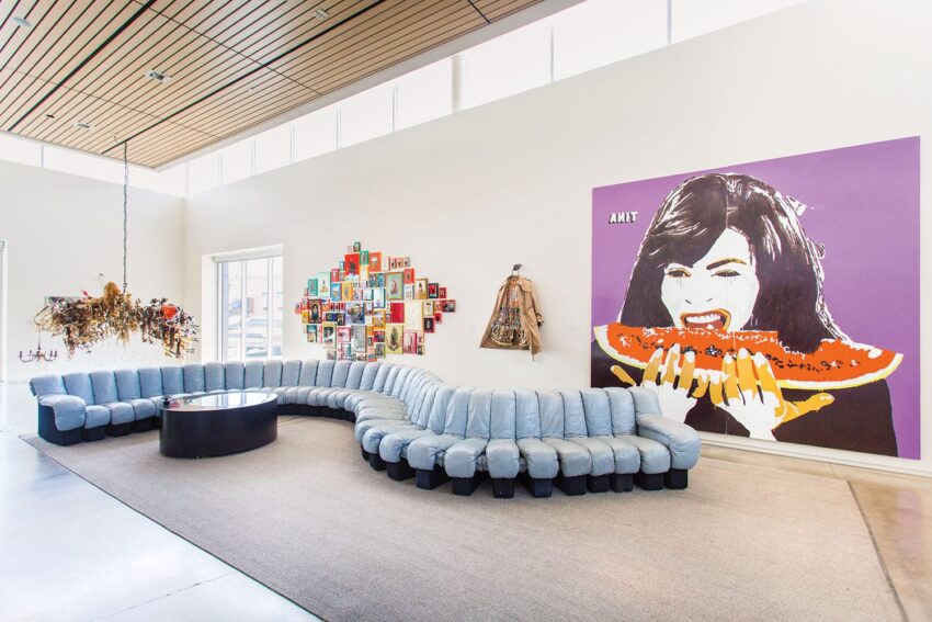 Modern living room with a large curved sofa, colorful wall art, and a purple artwork of a woman eating watermelon.
