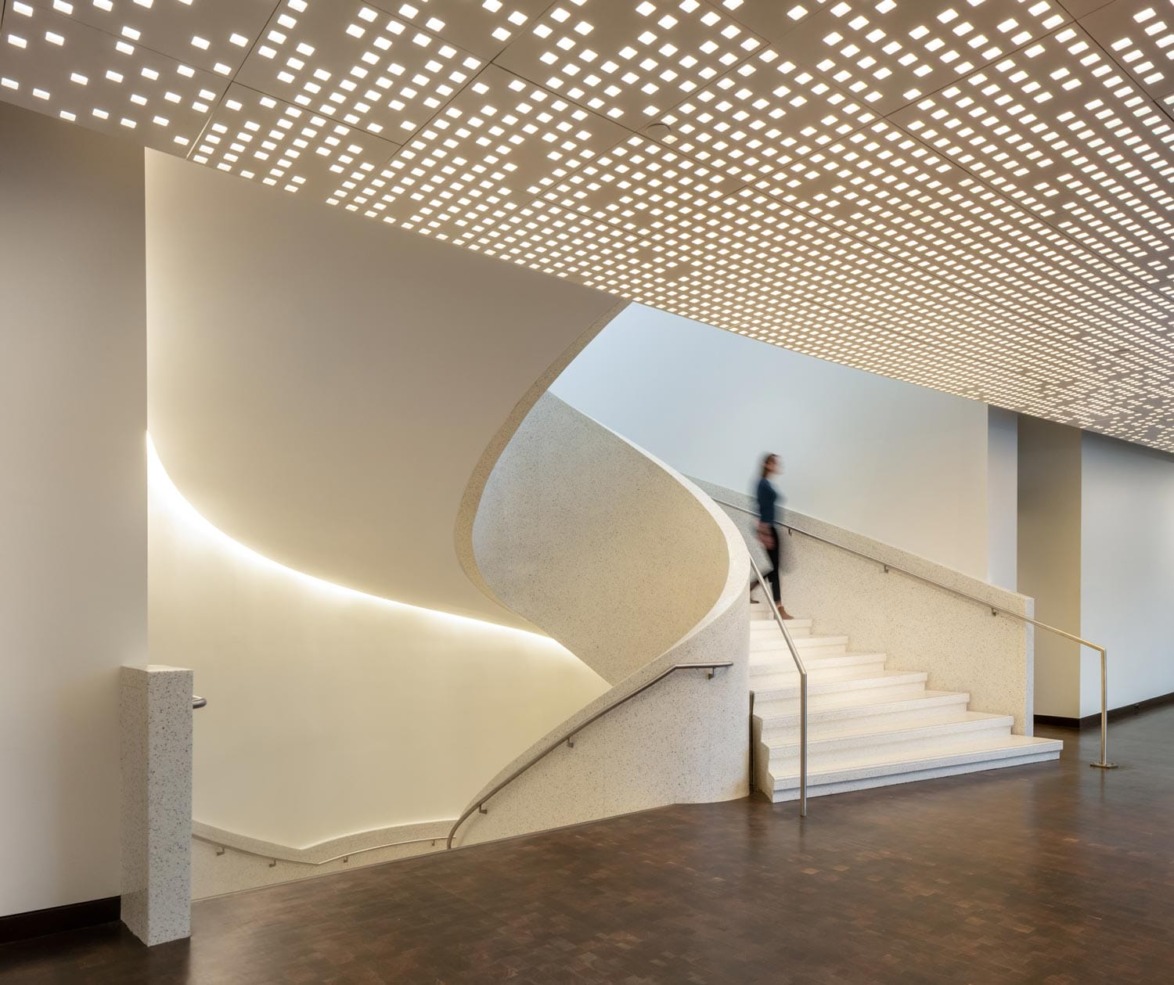 Modern interior with a curved staircase and patterned ceiling lights, featuring a blurred figure walking down the stairs.