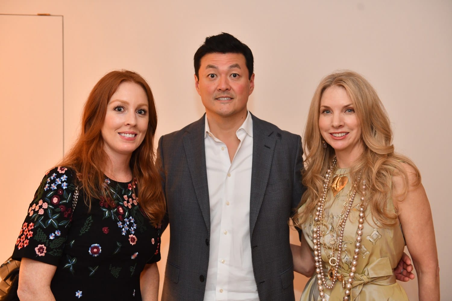 Three people posing together, two women and one man, dressed in formal attire against a neutral background.