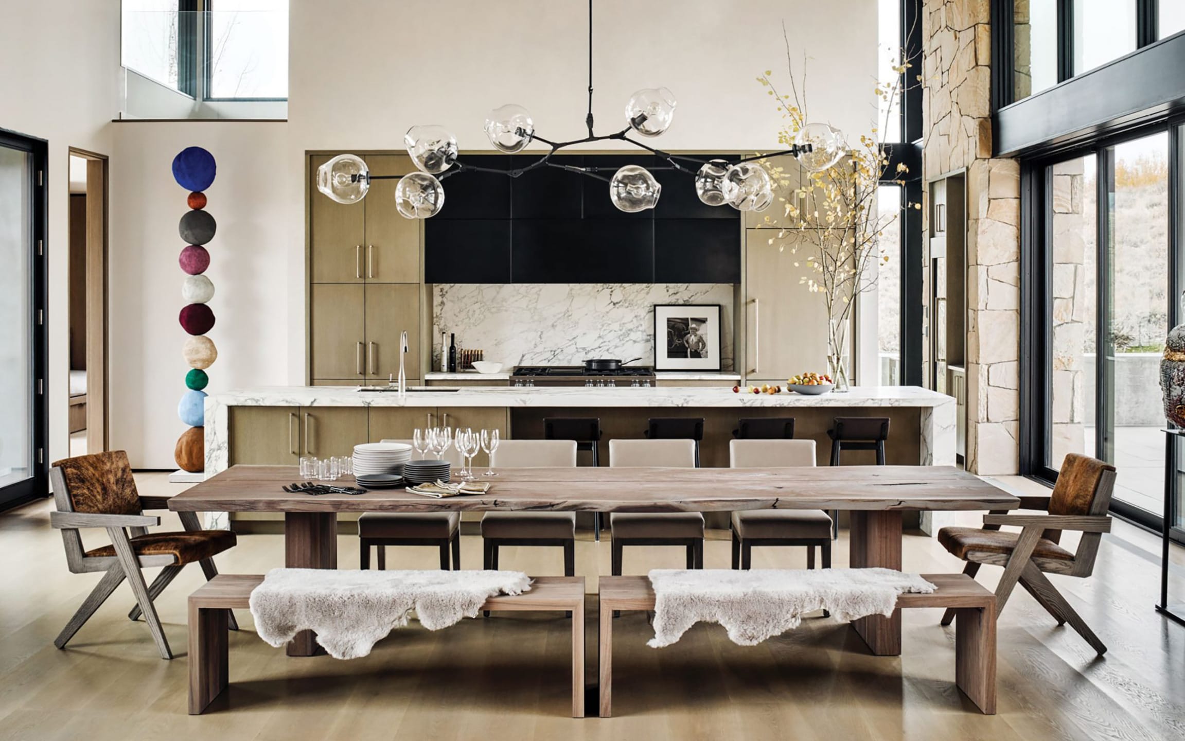 Modern kitchen with marble countertops, wooden dining table, benches, pendant light, and vibrant wall decor.