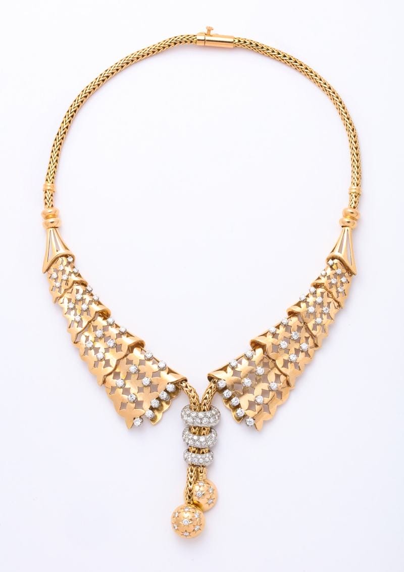 Gold necklace with intricate triangular links and gemstone accents, featuring spherical pendants on a white background.