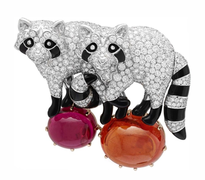 Two crystal-encrusted raccoon brooches holding red and orange gemstone spheres, designed with intricate details.