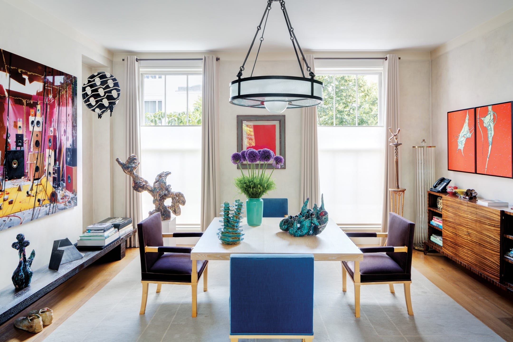Modern dining room with contemporary art, blue chairs, and a white table centered with decorative sculptures and a flower vase.