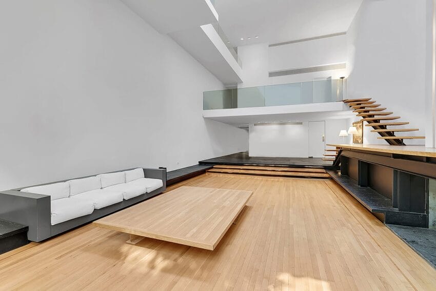Modern living room with high ceilings, wooden floors, a white sofa, minimalist staircase, and large coffee table.