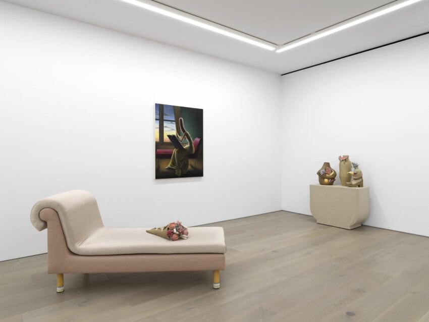 Art gallery with a modern beige chaise lounge, painting on white wall, and sculptures on a pedestal.
