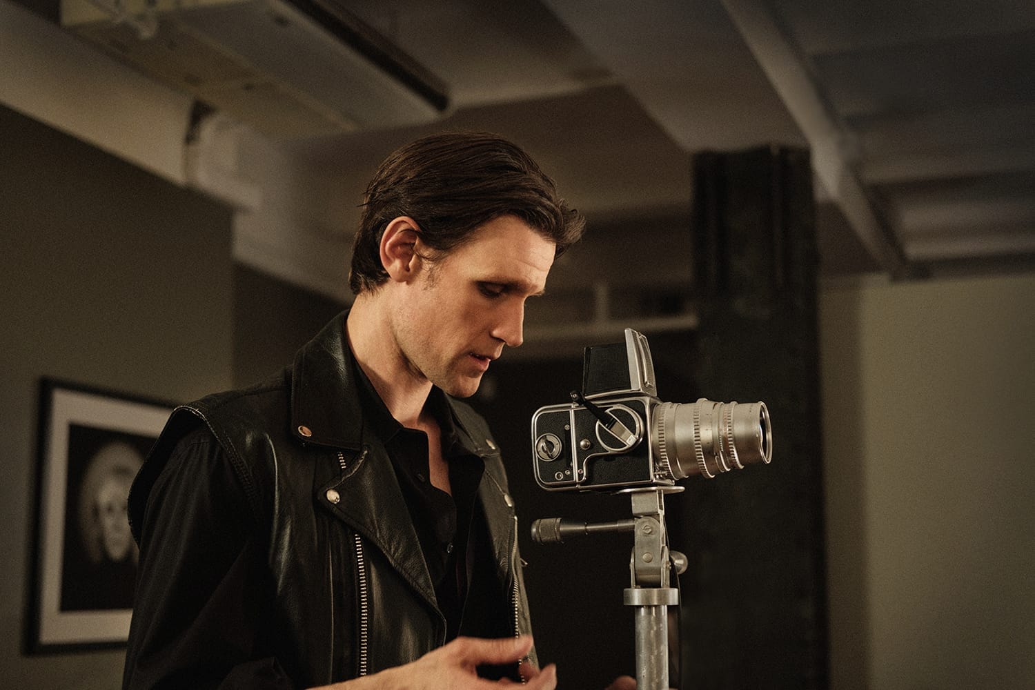 Person in a leather jacket operating a vintage camera on a tripod indoors.