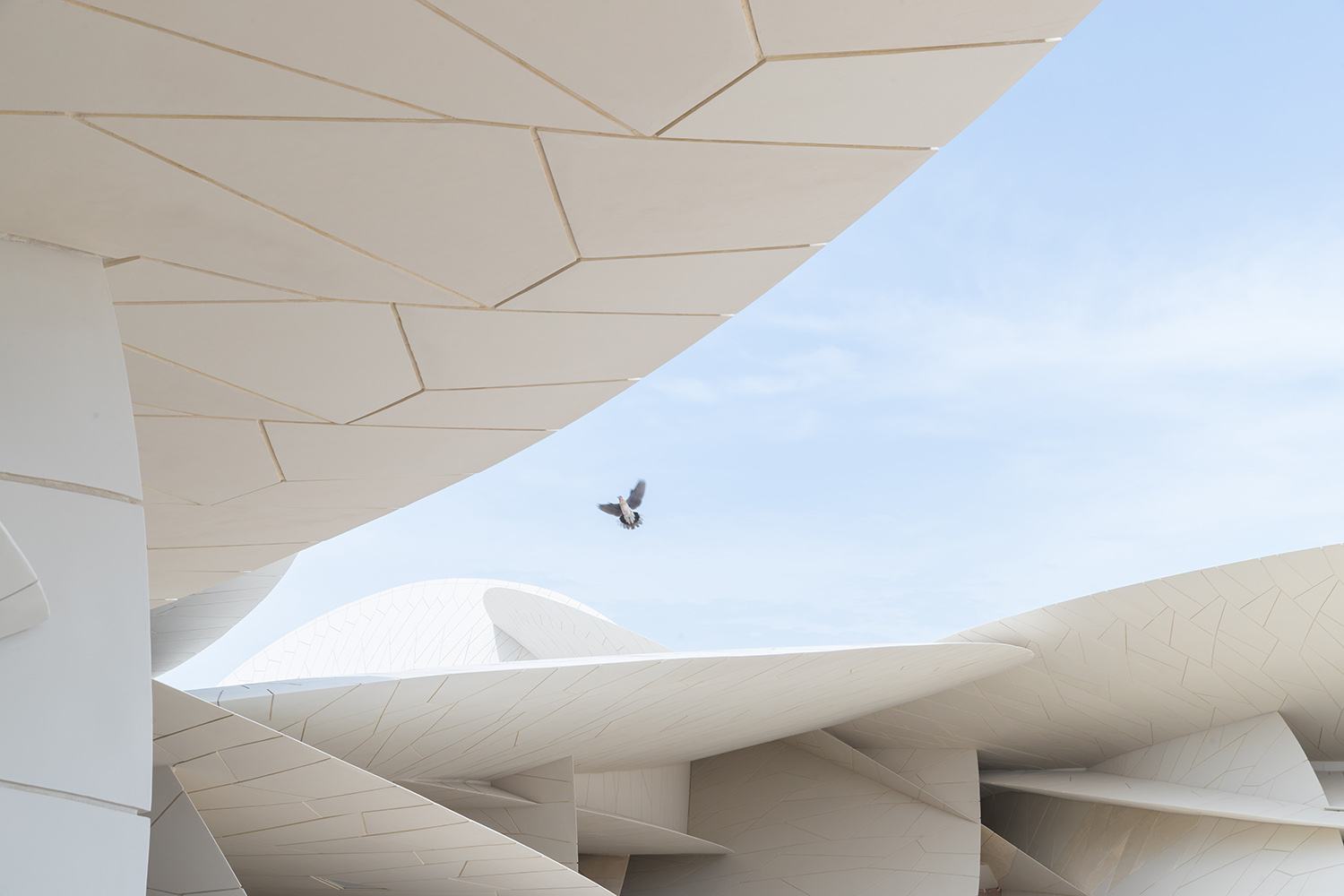 Modern architectural design with geometric shapes and a bird flying in a clear blue sky.