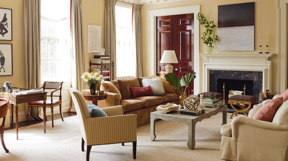 Elegant living room with cozy seating, a large window, art on walls, and a fireplace adorned with a plant and decor items.