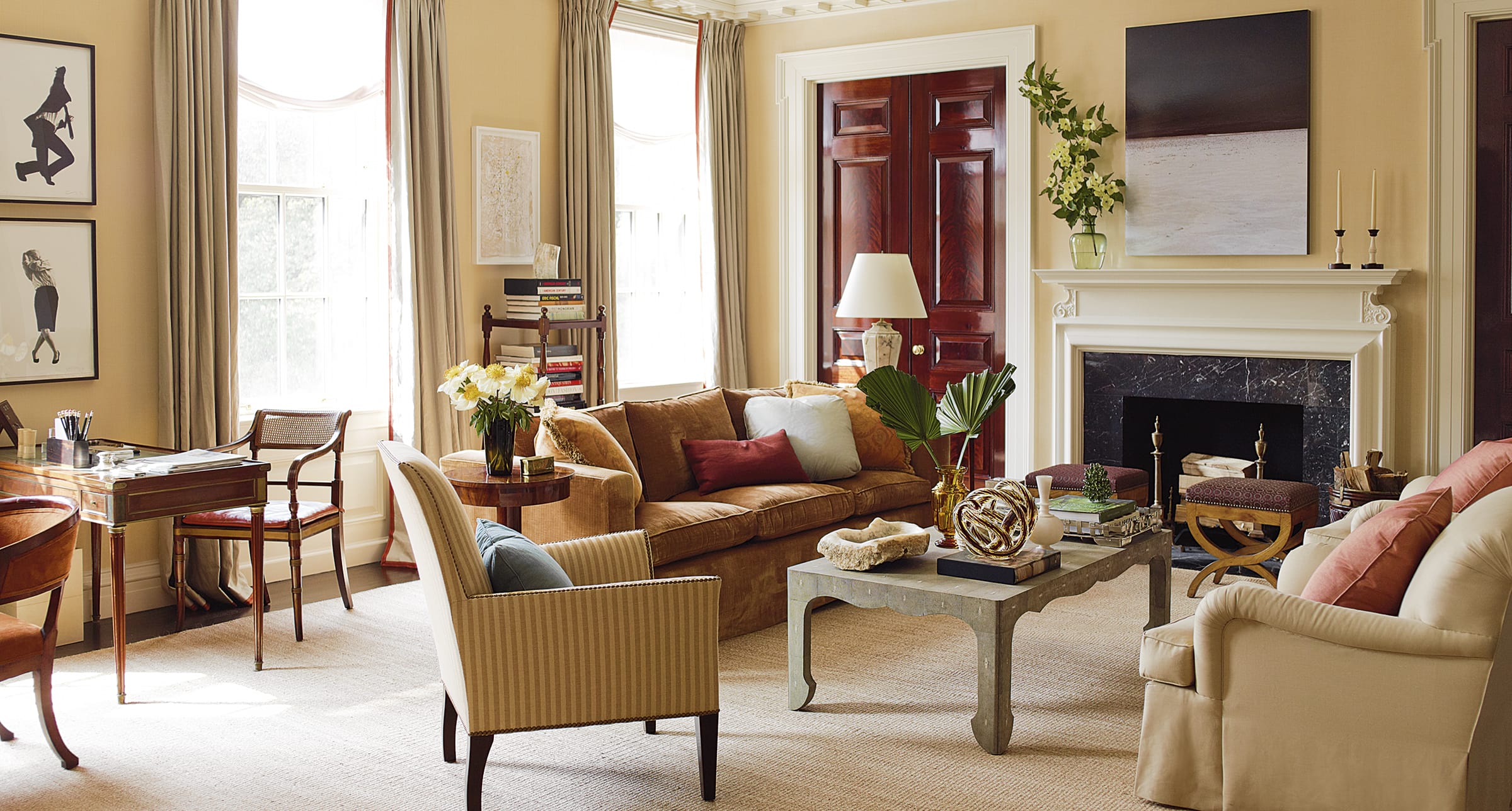 Elegant living room with cozy seating, a large window, art on walls, and a fireplace adorned with a plant and decor items.