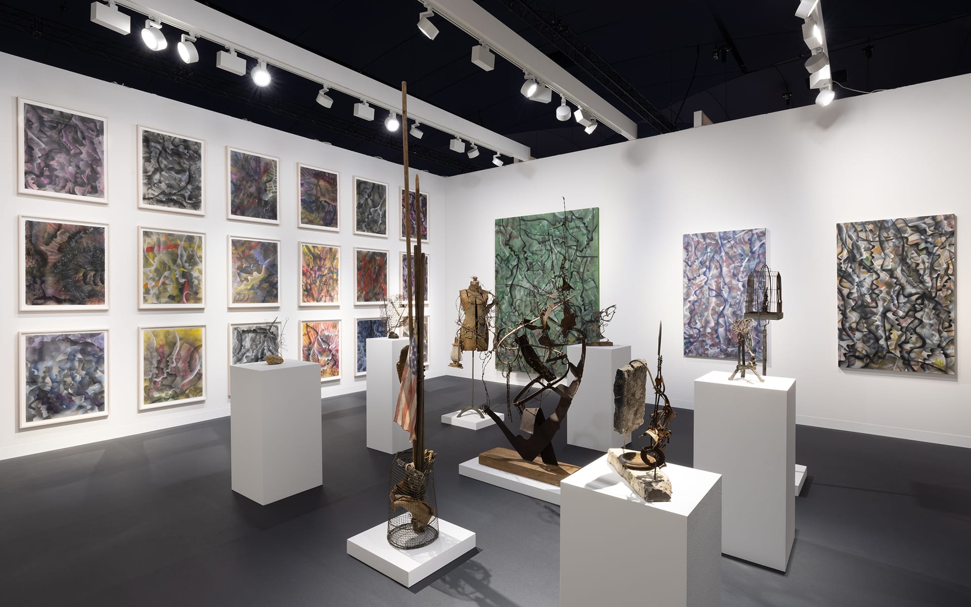Art gallery with abstract paintings and mixed media sculptures displayed on walls and pedestals in a well-lit room.