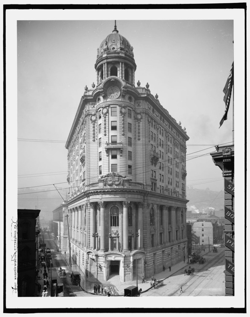 Historic Beaux-Arts style building with clock tower on a busy street corner, early 20th-century urban scene.