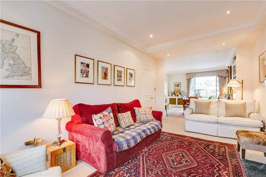 Cozy living room with red sofa, patterned rug, framed artwork on walls, and a view into a sunlit dining area.
